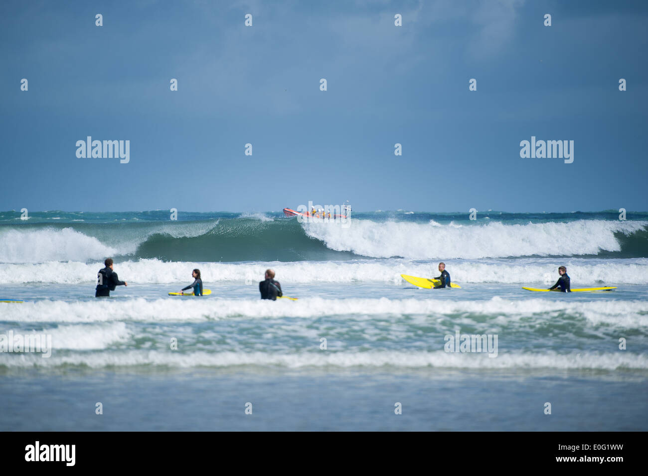 Surfer im Meer in Newquay, Cornwall, England. Ein RNLI Küstenwache Boot ist im Hintergrund hinter der brechenden Welle. Stockfoto