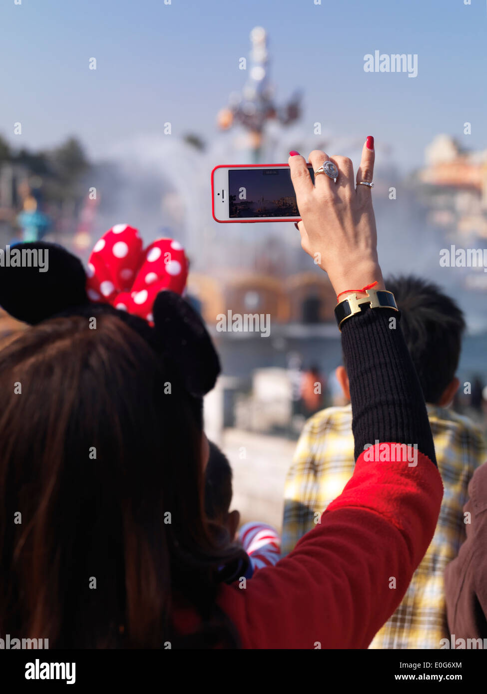 Frau, die Aufzeichnung einer Sendung mit ihrem iPhone im Tokyo Disneysea Themenpark. Japan. Stockfoto