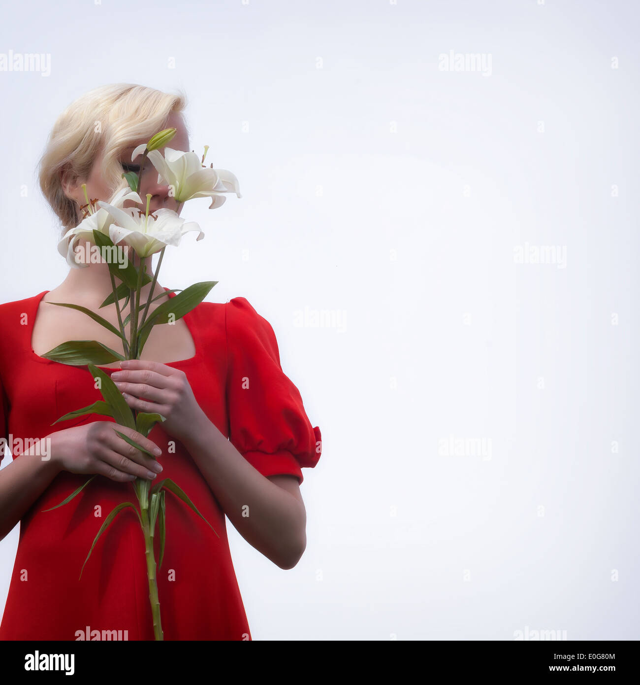 eine Frau in einem roten Kleid versteckt ihr Gesicht hinter weißen Lilien Stockfoto