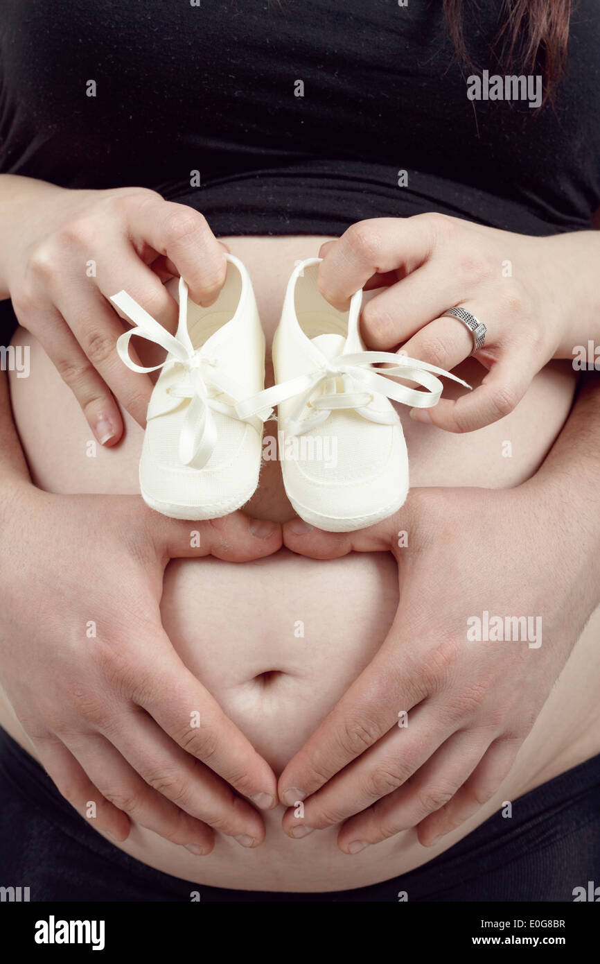 Schwangere Frau mit einem Kind Schuh, ihr Mann zärtlich hält ihren Bauch mit Herzform Stockfoto