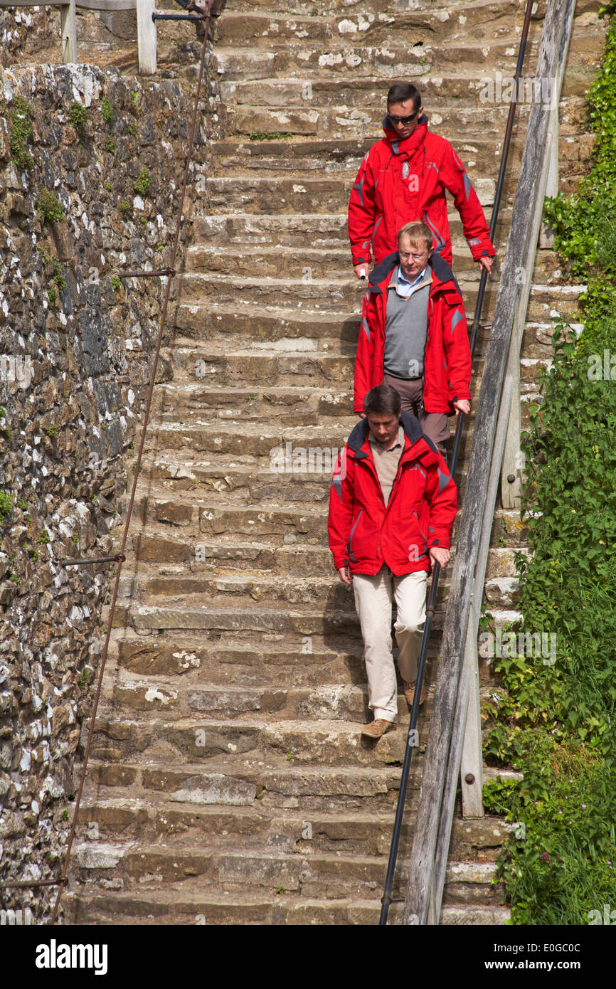 Das LEADER-Konzept - folgen drei Männer in roten Jacken steigen die Schritte auf Carisbrooke Castle, Carisbrooke, Newport, Isle of Wight, Hampshire Großbritannien im Mai Stockfoto