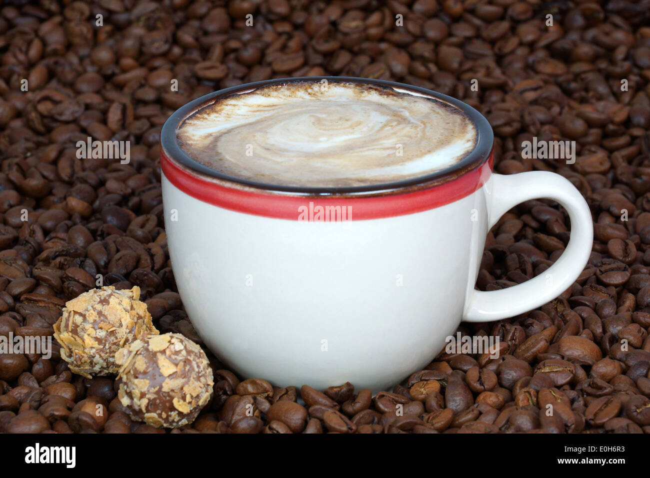 Tasse Kaffee und Süßigkeiten auf Kaffeebohnen Hintergrund Stockfoto