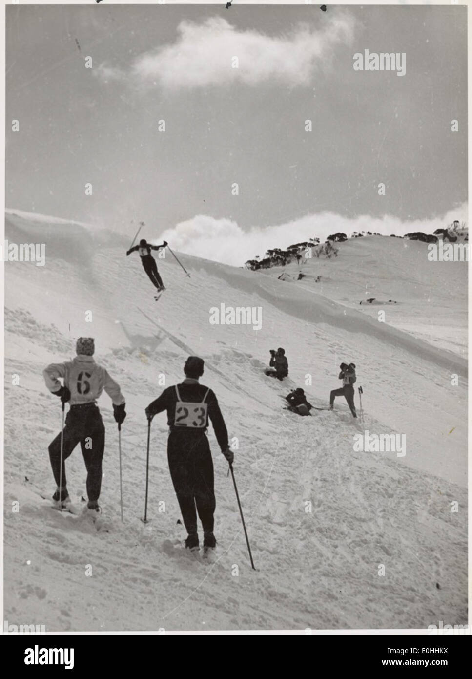 Männliche Skisprungfahrer beobachten einen Skifahrer, der einen Sprung auf den schneebedeckten Pisten, Snowy Mountains Region, New South Wales, Ca. 1942. Stockfoto