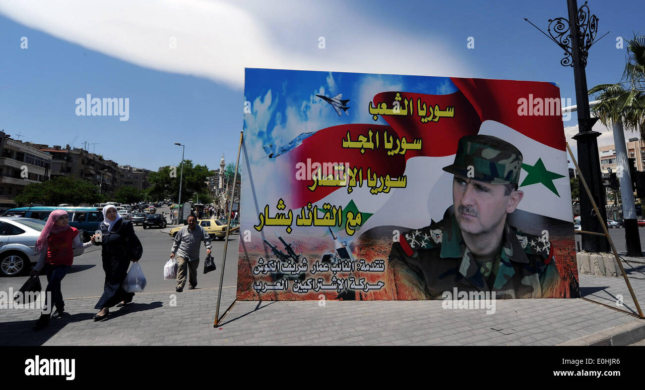 (140514)--Damaskus, 14. Mai 2014 (Xinhua)--Menschen vorbeigehen ein Wahl-Kampagne Plakat der amtierende Präsident Bashar al-Assad in Damaskus, die Hauptstadt Syriens, 13. Mai 2014. Poster und Banner von drei Präsidentschaftskandidaten Syriens schmücken die Hauptstraßen in Damaskus, mit Amtsinhaber Präsident Bashar al-Assad vorhersagbar erhält den Löwenanteil der Publizität, als Wahlkampf für die Wahlen am 12. Mai beginnen. Syriens Obersten Verfassungsgericht akzeptiert die Kandidatur von drei Anwärter, einschließlich nämlich Maher Hammerle Hajjar, Hassan Abdullah al-Nouri und Baschar al-Assad, für t Stockfoto