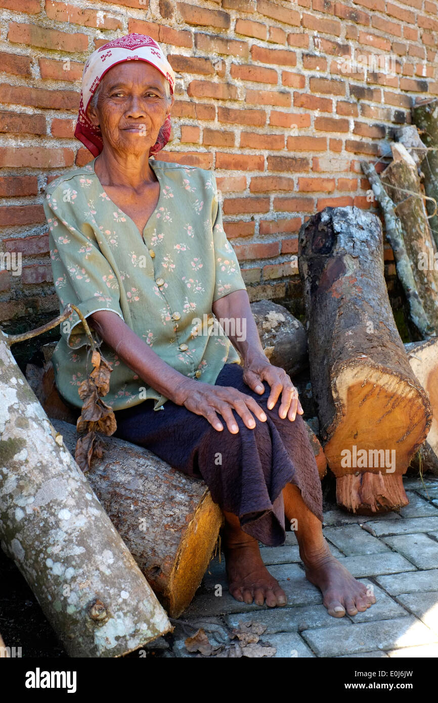 ältere Dame mit grauem Star vergeht die Zeit saß auf einem Haufen von Protokollen in einem ländlichen Dorf in Ost-Java-Indonesien Stockfoto