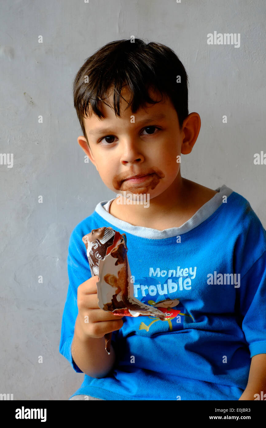kleiner Junge ein Schokoladeneis zu essen und immer das meiste davon über sein Gesicht verschmiert Stockfoto