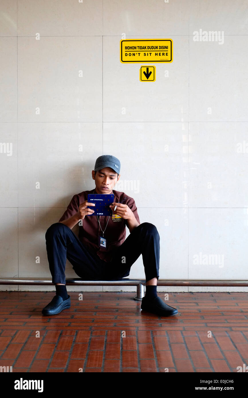 ein Arbeiter am Flughafen Soekarno Hatta in Jakarta Indonesien nimmt sich eine Auszeit, die unter Zeichen, das sagt nicht hier sitzen Stockfoto