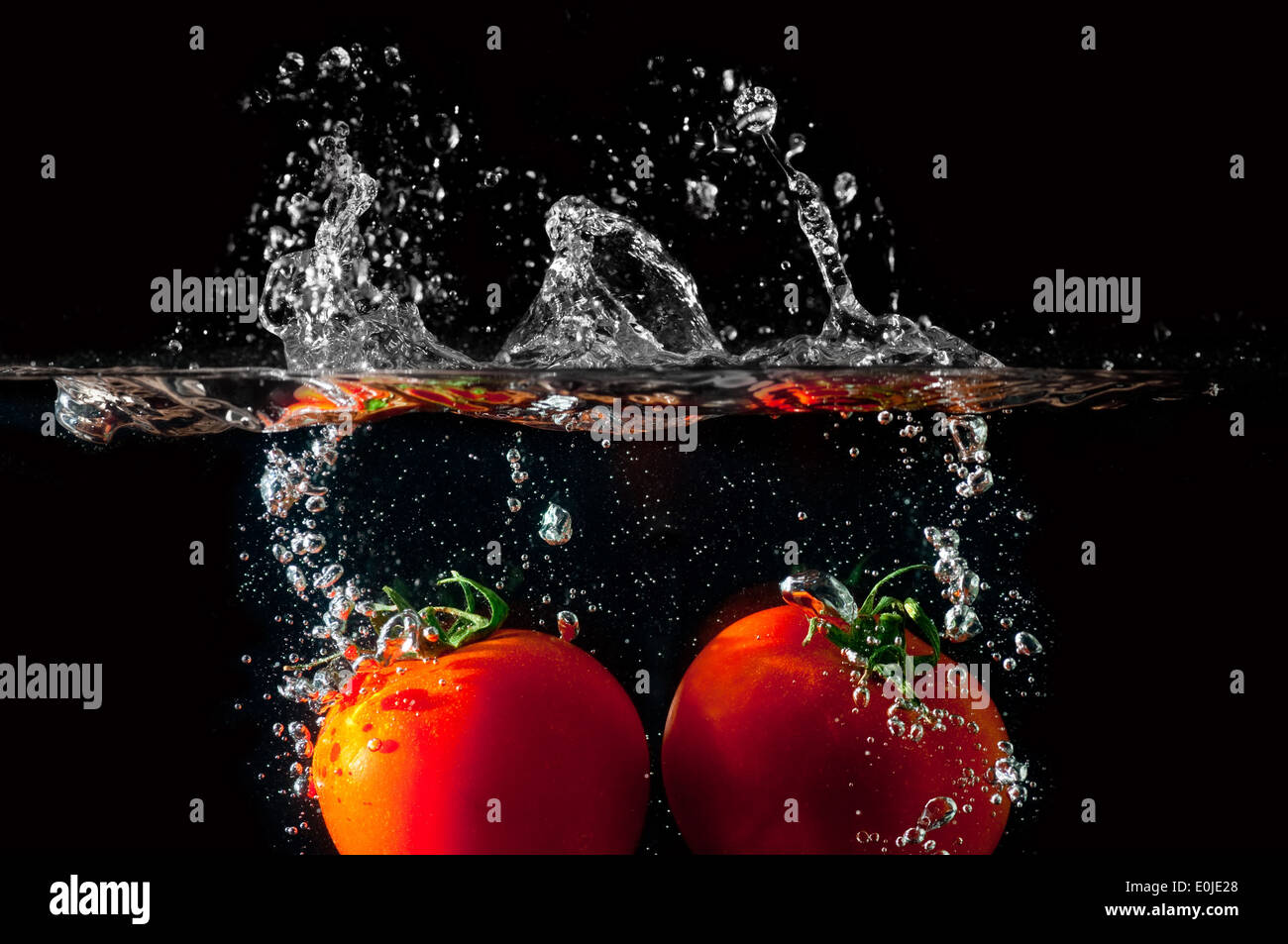 Zwei Tomaten fallen ins Wasser vor schwarzem Hintergrund Stockfoto