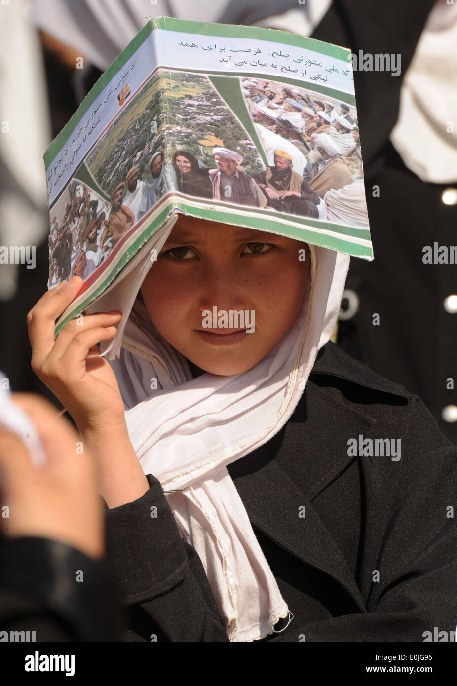 Ein afghanisches Mädchen verwendet ein Schulbuch, um ihre Augen vor der Sonne Schatten, wie sie für eine erste Spatenstich Zeremonie zu Beginn der Al wartet Stockfoto