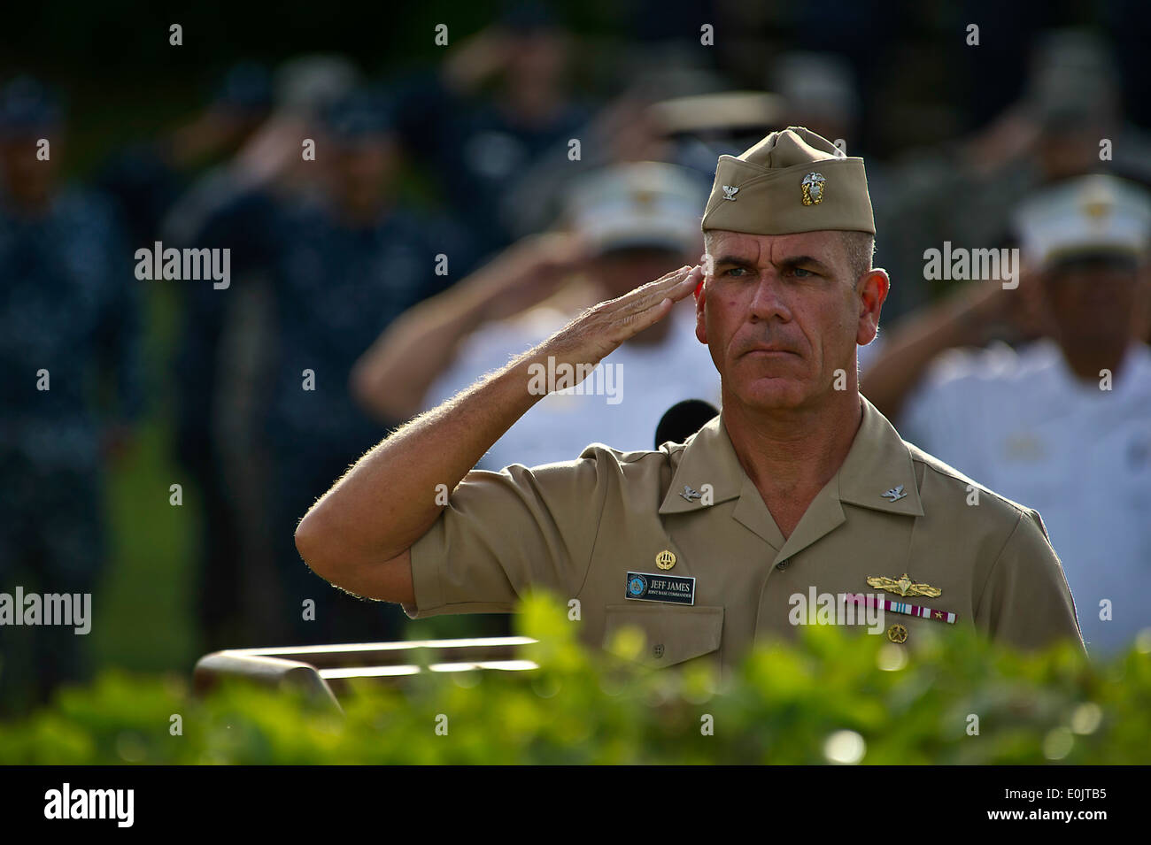 US Navy Captain Jeffery James, gemeinsame Basis Pearl Harbor-Hickam Kommandant salutiert, wie die amerikanische Flagge, die Hälfte Mitarbeiter ausgelöst wird ein Stockfoto