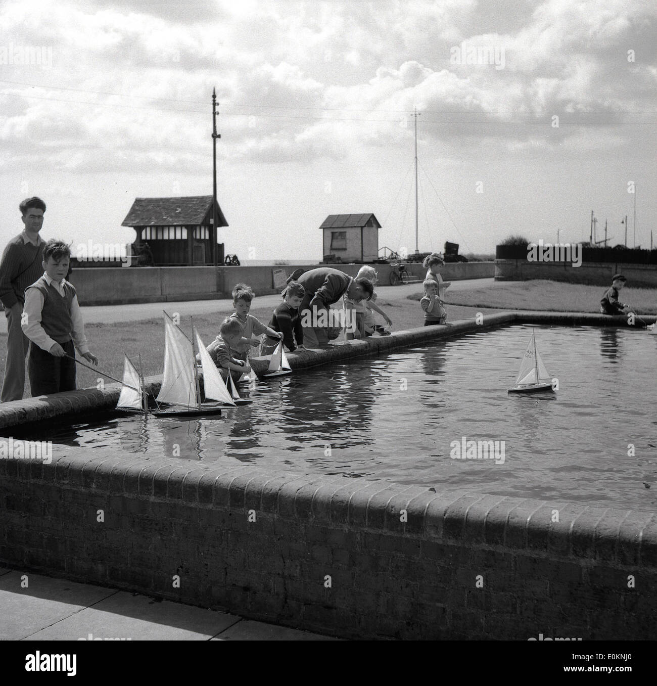 1950er Jahren Geschichtsbild der Kinder spielt mit ihrem Spielzeug Segelboote auf einen kleinen Mann--made Modell See oder Teich. Stockfoto