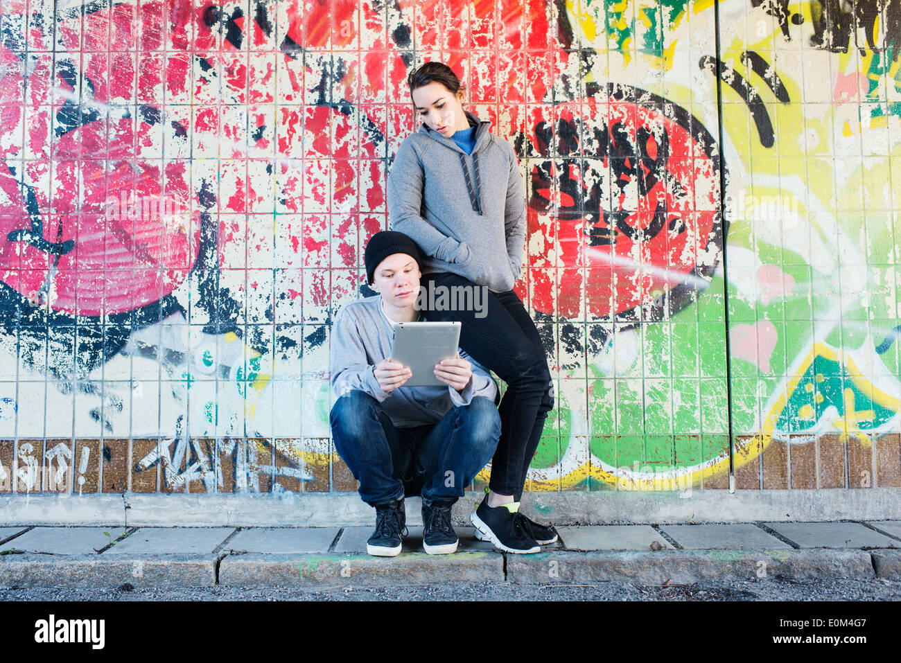 Porträt des lockeren und entspannten junger Mann und Frau liest auf einem Notizblock vor Graffiti-Wand im Stadtgebiet. Stockfoto