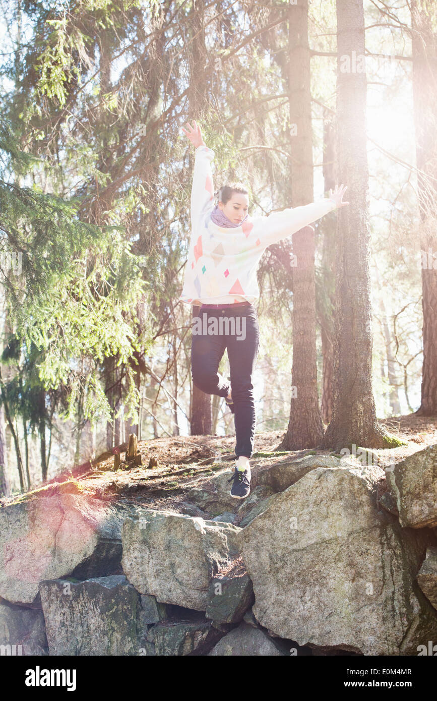Junge Frau in der Natur am Rande des großen Felsen im Wald springen. Stockfoto