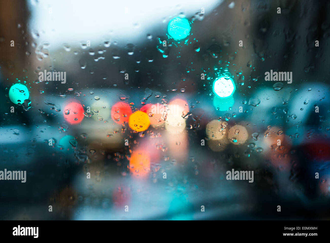 Unscharfes Licht des Autos gesehen durch einen nassen Windschutzscheibe mit einigen Regentropfen auf es in den frühen Morgenstunden von einem regnerischen Tag Stockfoto