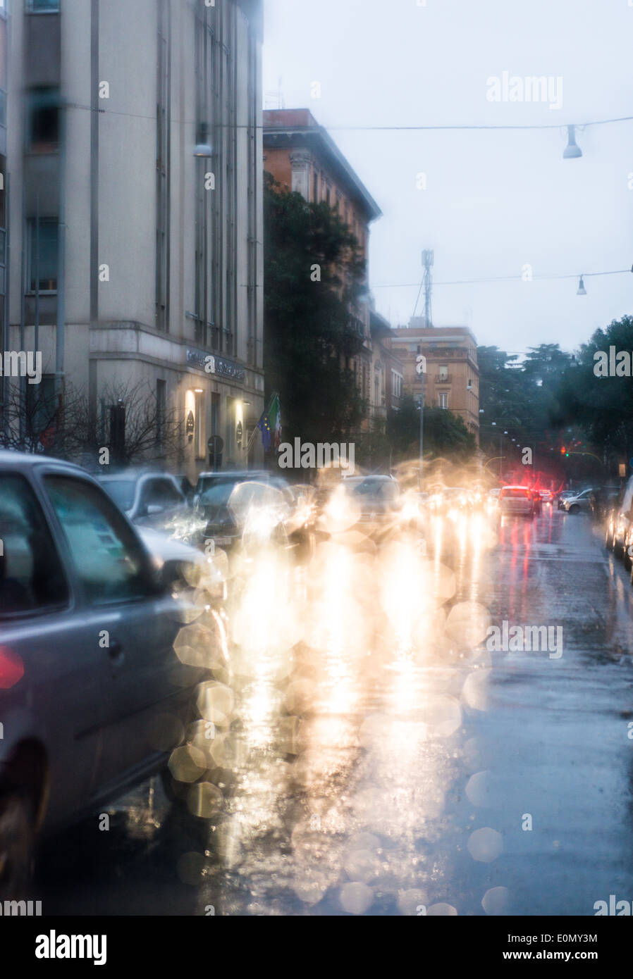 Unscharfes Licht des Autos gesehen durch einen nassen Windschutzscheibe mit einigen Regentropfen auf es in den frühen Morgenstunden von einem regnerischen Tag Stockfoto