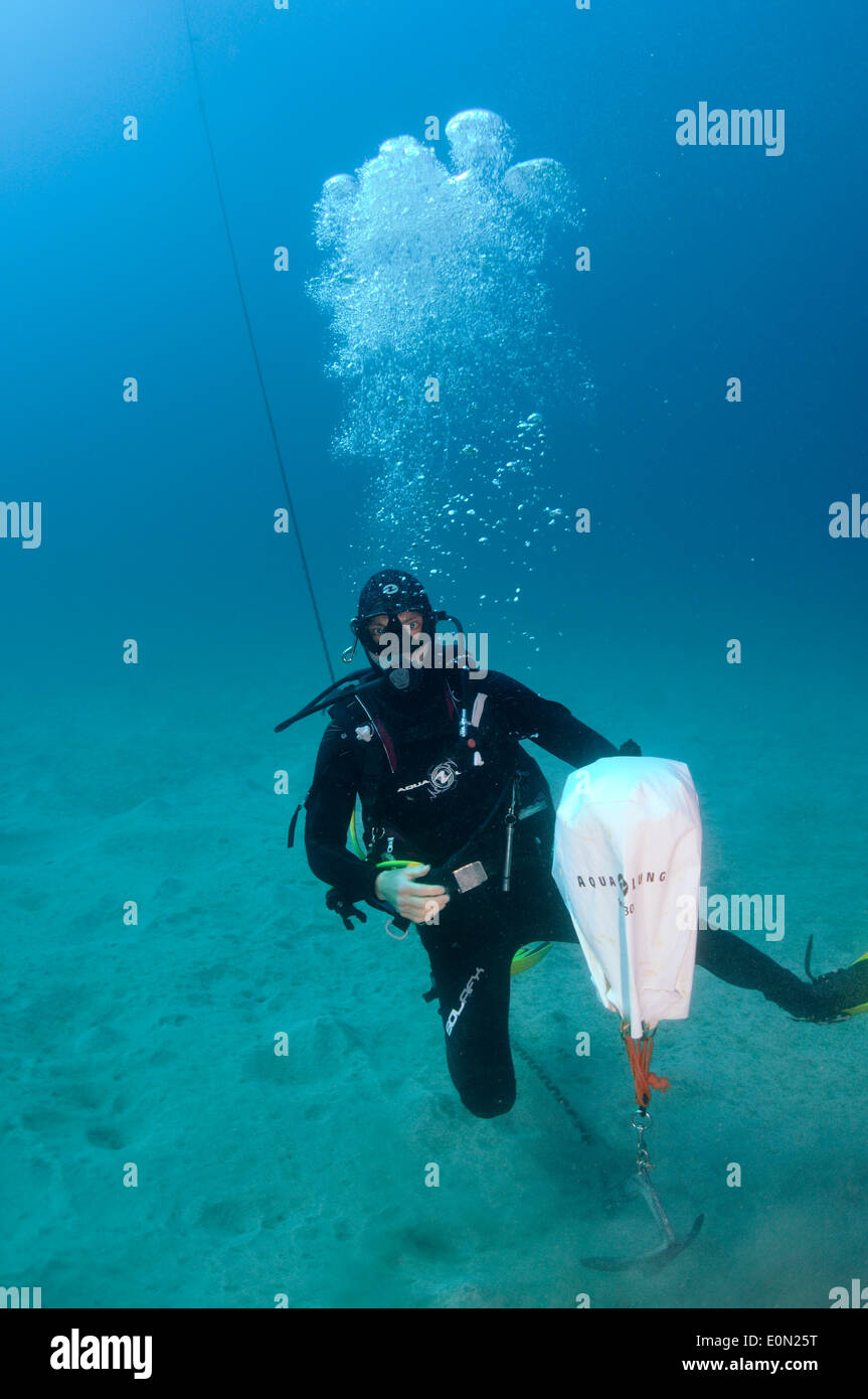 Scuba Diver auf sandigen Meeresboden Einrichtung heben Tasche, Anker zu heben Stockfoto