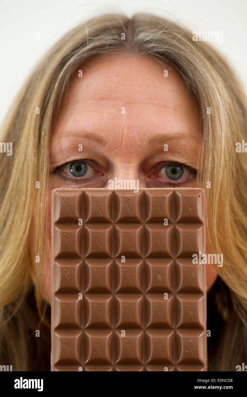 Eine Dame mittleren Alters eine Tafel Schokolade vor ihr Gesicht halten. Stockfoto