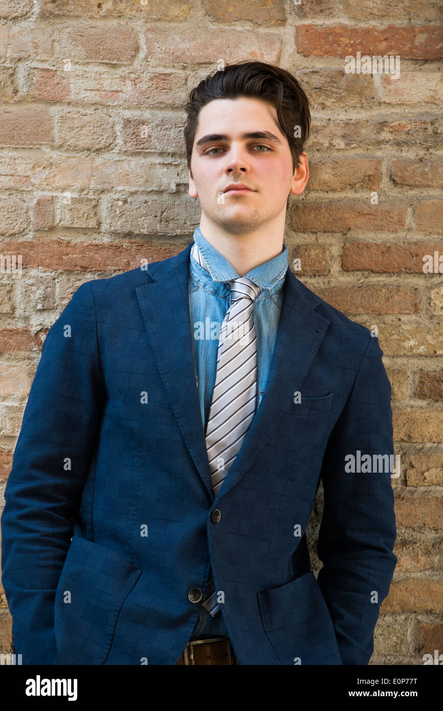 Hübscher junger Mann im Anzug gegen Mauer, die Hände in den Taschen, Blick in die Kamera Stockfoto