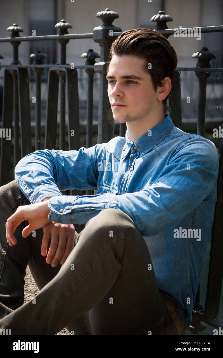 Hübscher junger Mann sitzen gegen Handlauf im Freien, ernsten Ausdruck Stockfoto