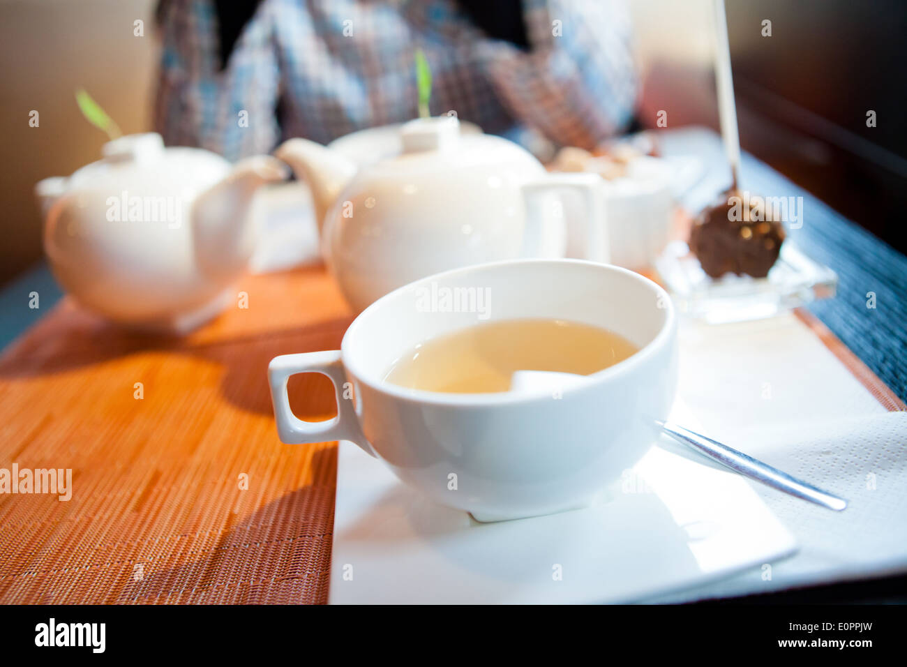 Nahaufnahme der Tasse Kräutertee mit Teekannen und Frau im Hintergrund Stockfoto