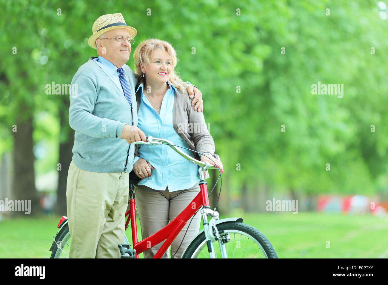 Älteres paar umarmt und schob ein Fahrrad im park Stockfoto