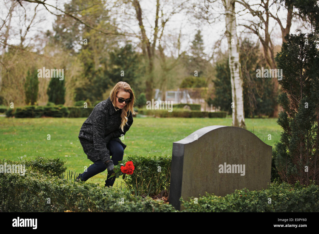 Junge Frau, die Blumen auf dem Grab eines verstorbenen Familienmitglieds am Friedhof zu platzieren. Junge Dame auf dem Friedhof, die Ehre erweisen. Stockfoto