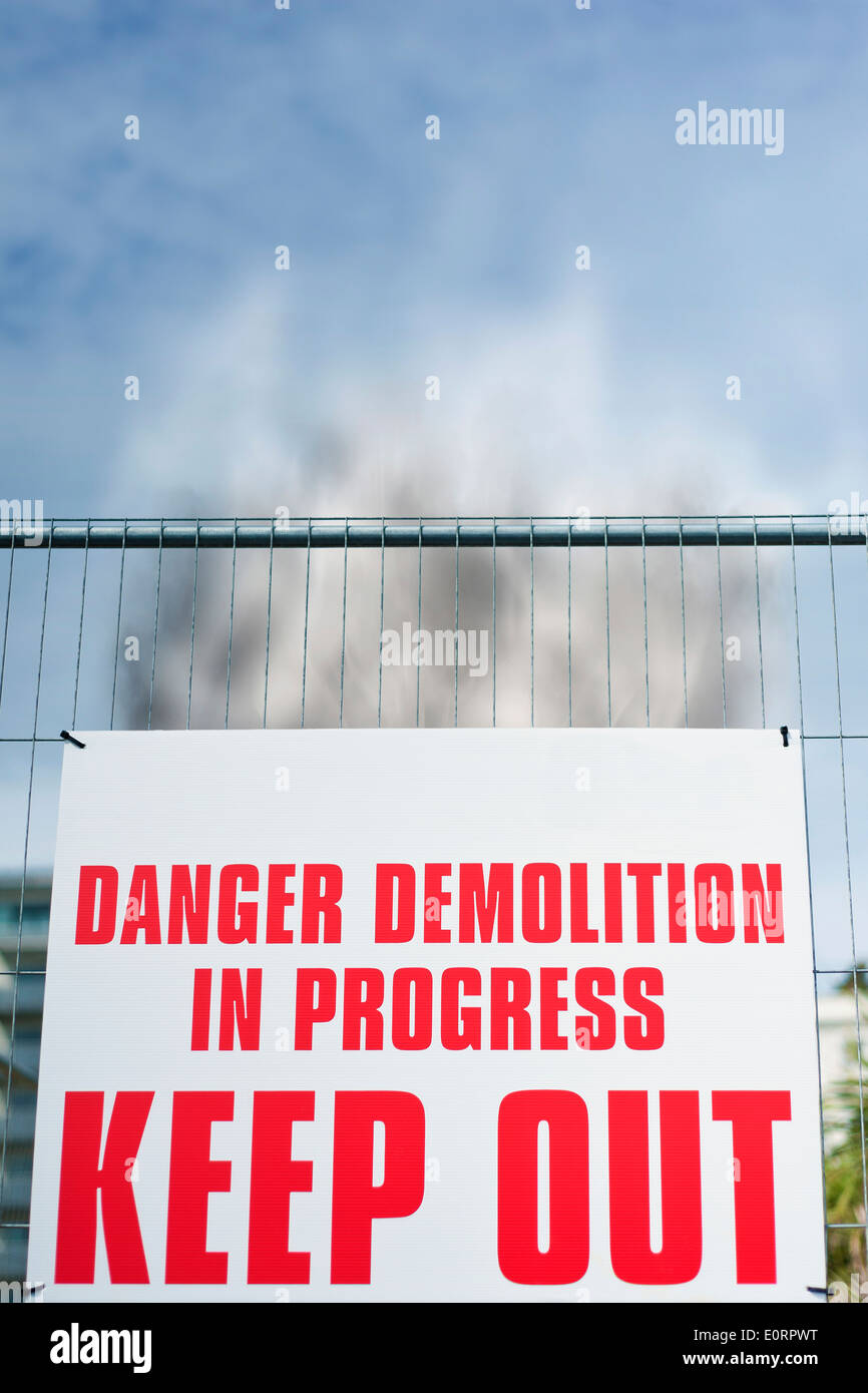 Warnung Schild 'Danger Abriss im Gange halten OUT' auf einer Baustelle mit steigenden Rauch hinter sich, Großbritannien Stockfoto