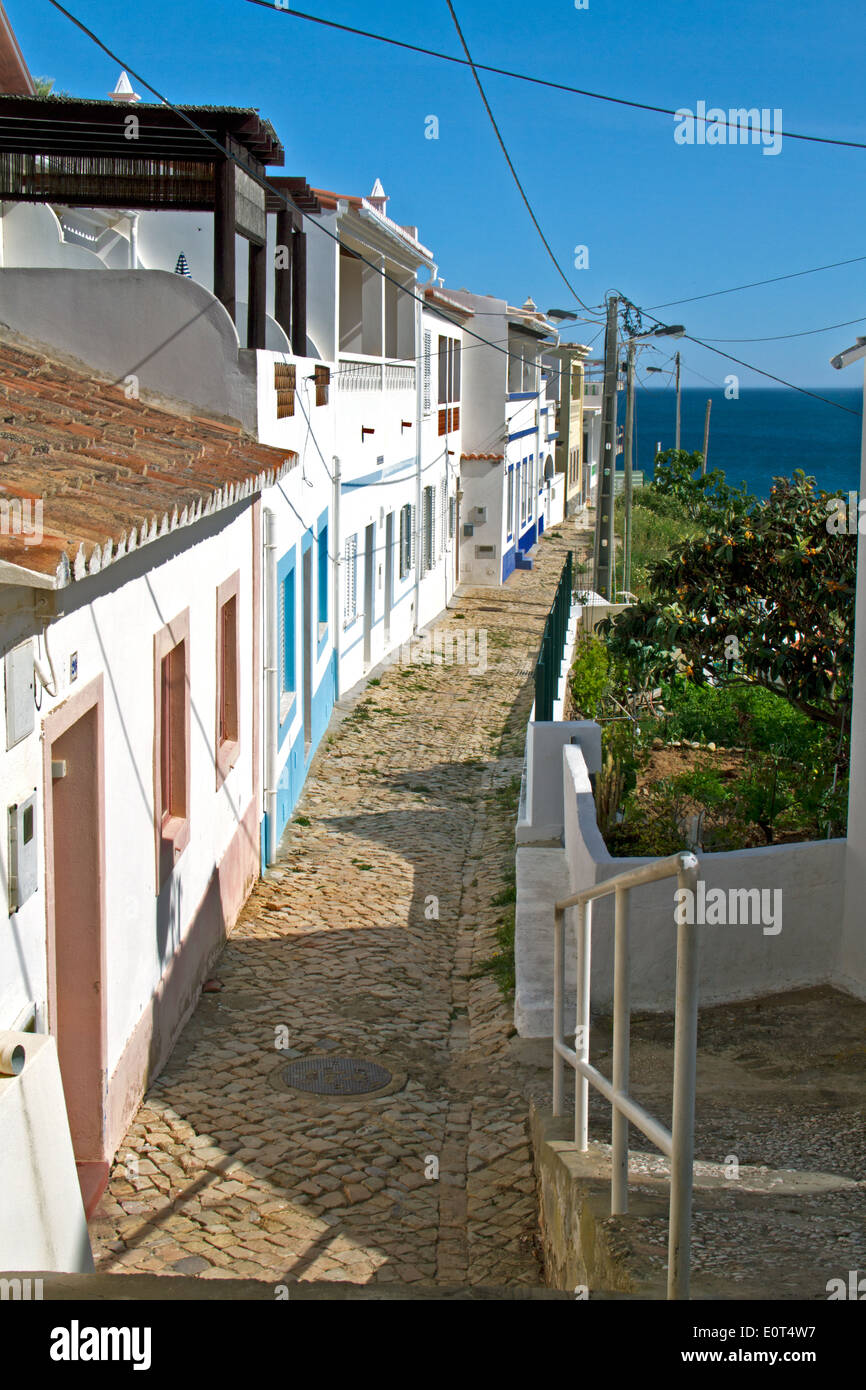 Kleine Straße mit weißen Häusern und Kopfsteinpflaster in dem Fischerdorf Salema, Algarve, Portugal Stockfoto