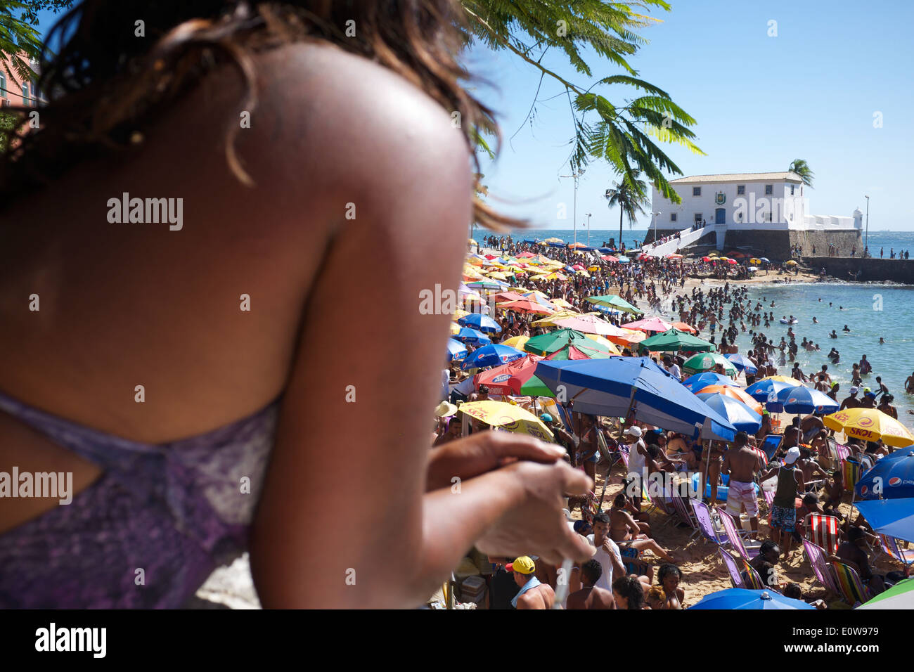 SALVADOR, Brasilien - 13. Oktober 2013: Brasilianische Frau blickt über Massen von Menschen entspannen am Strand von Porto da Barra, Stockfoto