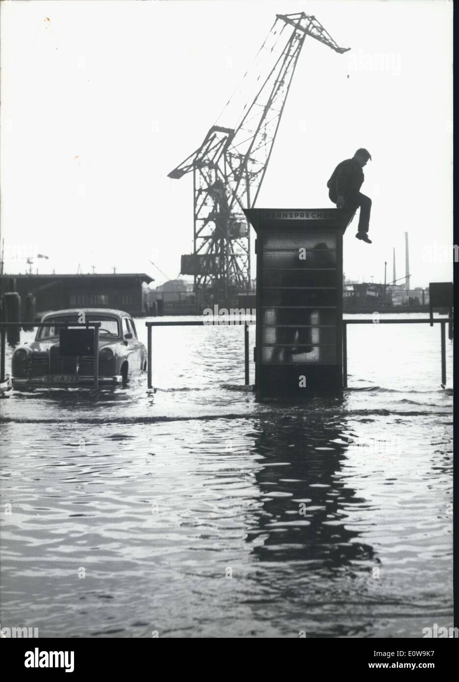 19. Februar 1962 - Wasser überall: Es gibt keinen trockenen Weg für so junge Mann sitzt auf dem Dach des ein "Telefonzelle in der zwei Menschen versuchen, ihre Verwandten nennen, die vergeblich in den schlimmsten Fall beschädigte Bezirk von Hamburg.however Leben. Stockfoto