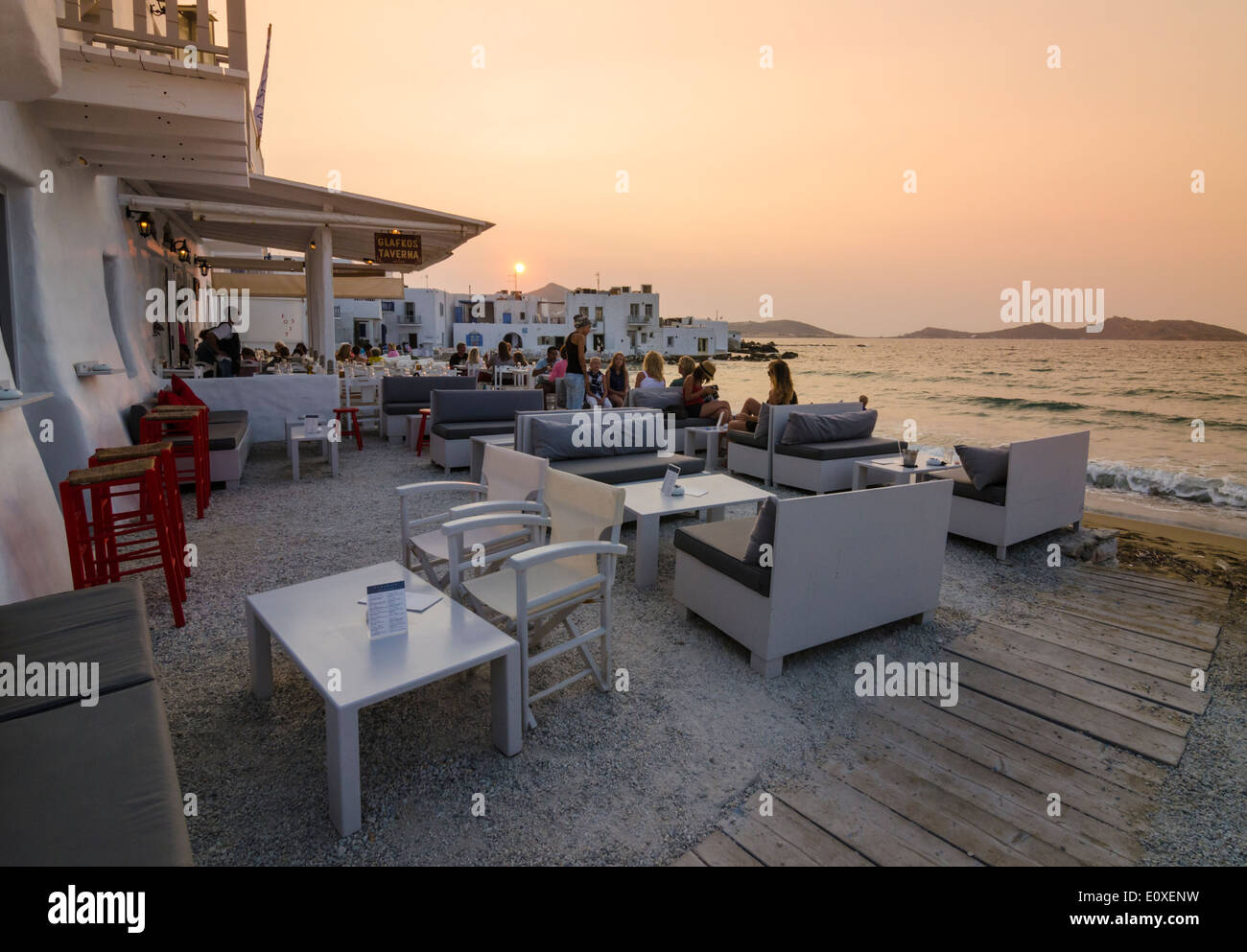Menschen sitzen in einem Café am Meer bei Sonnenuntergang in Naoussa, Paros, Griechenland Stockfoto