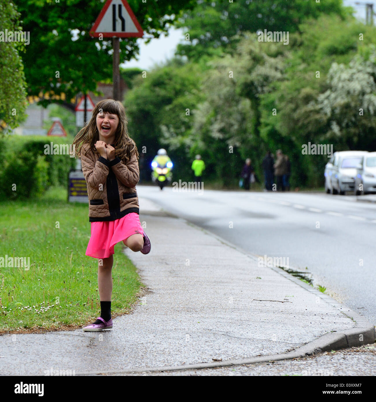 Junge weiße Mädchen mit langen braunen Haaren in einem rosa Rock und braune Jacke auf der Straße im Regen tanzen. Manningtree, UK Stockfoto