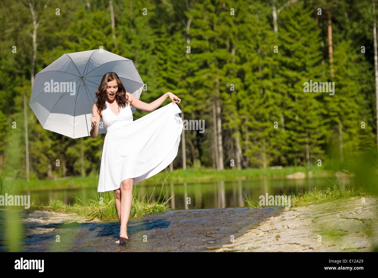 5. Juni 2010 - 5. Juni 2010 - Happy romantische Frau mit Sonnenschirm in der Sonne, weißen Kleid, zu Fuß in Wasser Stockfoto