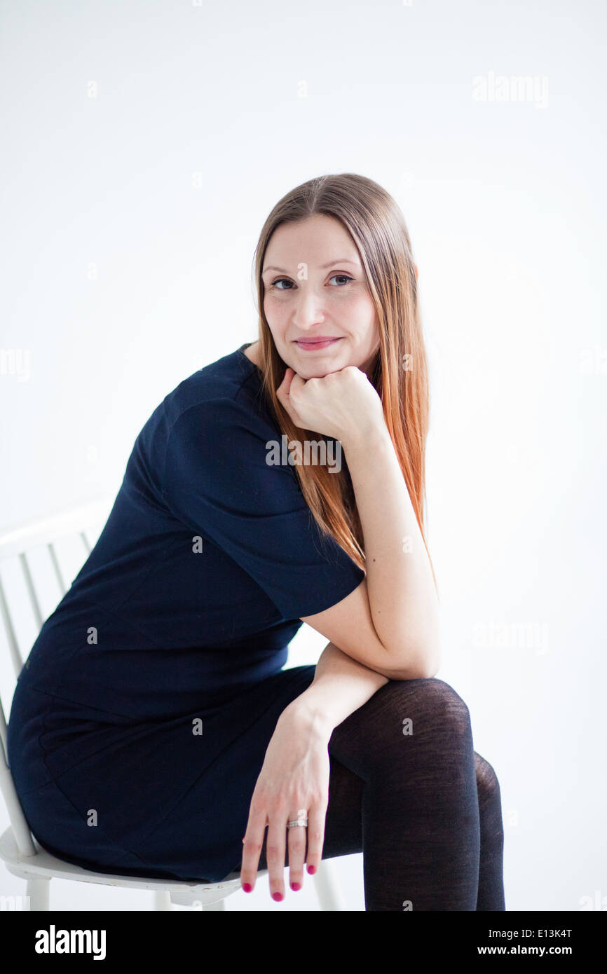 Studioportrait glücklich lächelnde attraktive Frau tragen blaue Bluse und im Stuhl sitzen und ausruhen Kinn auf Seite Stockfoto