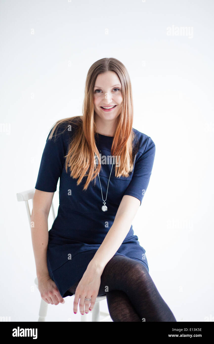 Studioportrait glücklich lächelnd attraktive Frau tragen blaue Bluse und sitzen auf Stuhl Stockfoto