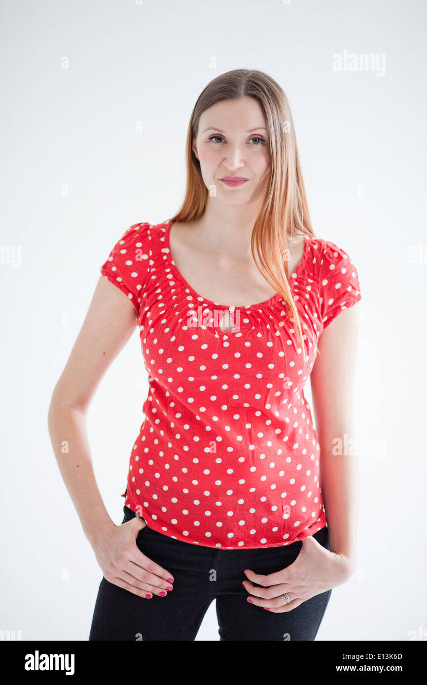 Studio-Porträt der attraktive Frau mit glücklich Grinsen und tragen rote Bluse und Stand mit Hände auf den Hüften Stockfoto