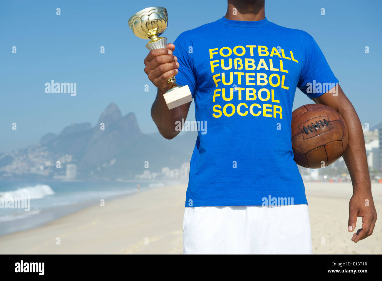 Champion brasilianischer Fußballspieler holding Trophy und Vintage Fußball im internationalen Fußball T-shirt Ipanema Strand Rio Stockfoto