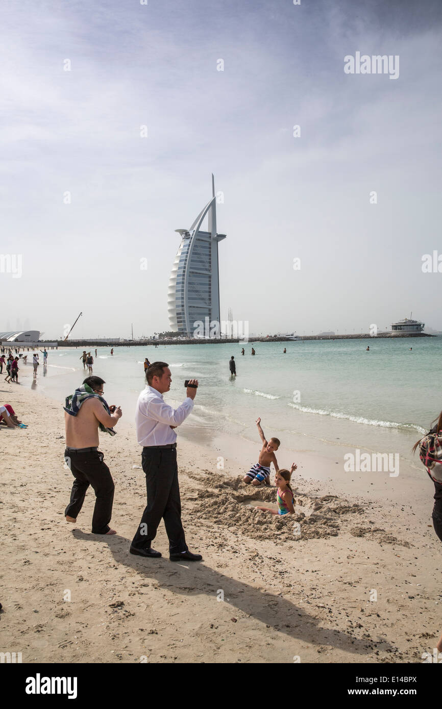Vereinigte Arabische Emirate, Dubai, Burj Al Arab Hotel. Asiatische Touristen nimmt Bilder der kaukasischen Kinder am Strand Stockfoto