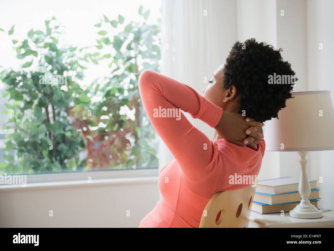 Schwarze Frau entspannend am Fenster mit Händen hinter dem Kopf Stockfoto