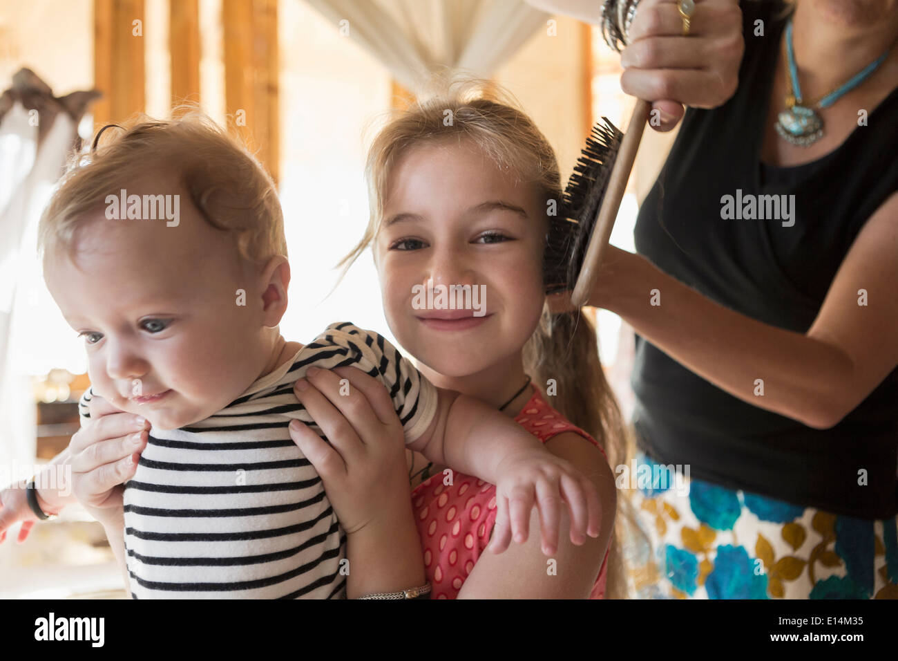 Kaukasische Mädchen Holding Bruder als Mutter ihr Haar Bürsten Stockfoto