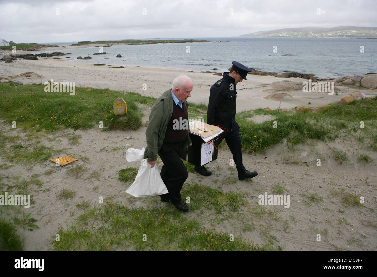 Vorsitzender Offizier Hugh O'Donnell und Garda Officer p.j. McHugh tragen die Wahlurne auf der Insel Innishfree, County Donegal, Stockfoto