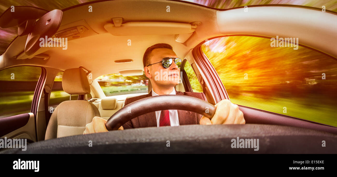 Mann in einem Anzug und Sonnenbrille auf einer Straße im Auto fahren. Stockfoto