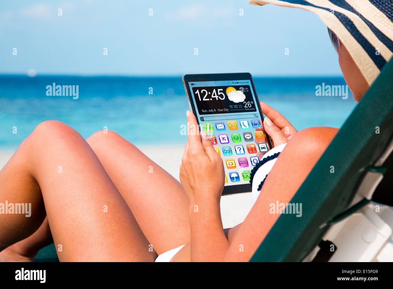 Frau im Urlaub liegt auf einer Sonnenliege am Strand mit einem Tablet in Händen. Stockfoto