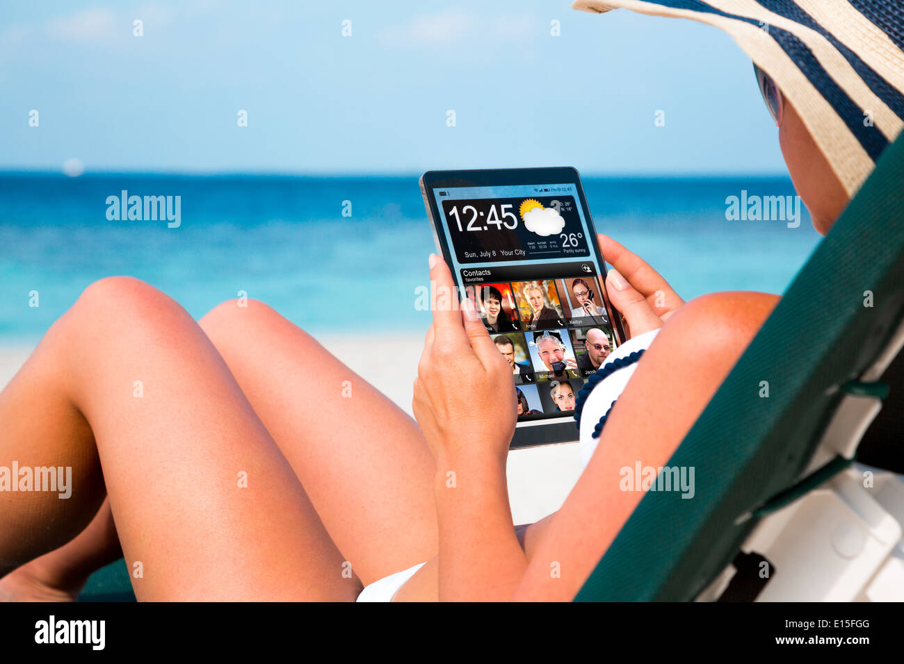 Frau im Urlaub liegt auf einer Sonnenliege am Strand mit einem Tablet in Händen. Stockfoto