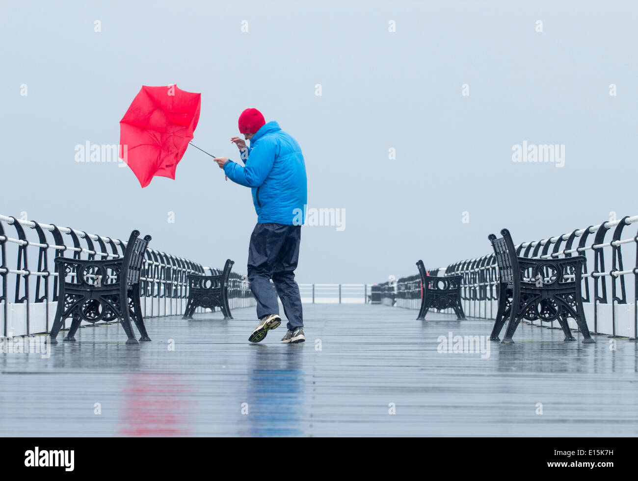 Mann kämpft mit Regenschirm auf Saltburn viktorianischen Pier in strömendem Regen. Saltburn durch das Meer, North Yorkshire, England. UK Stockfoto