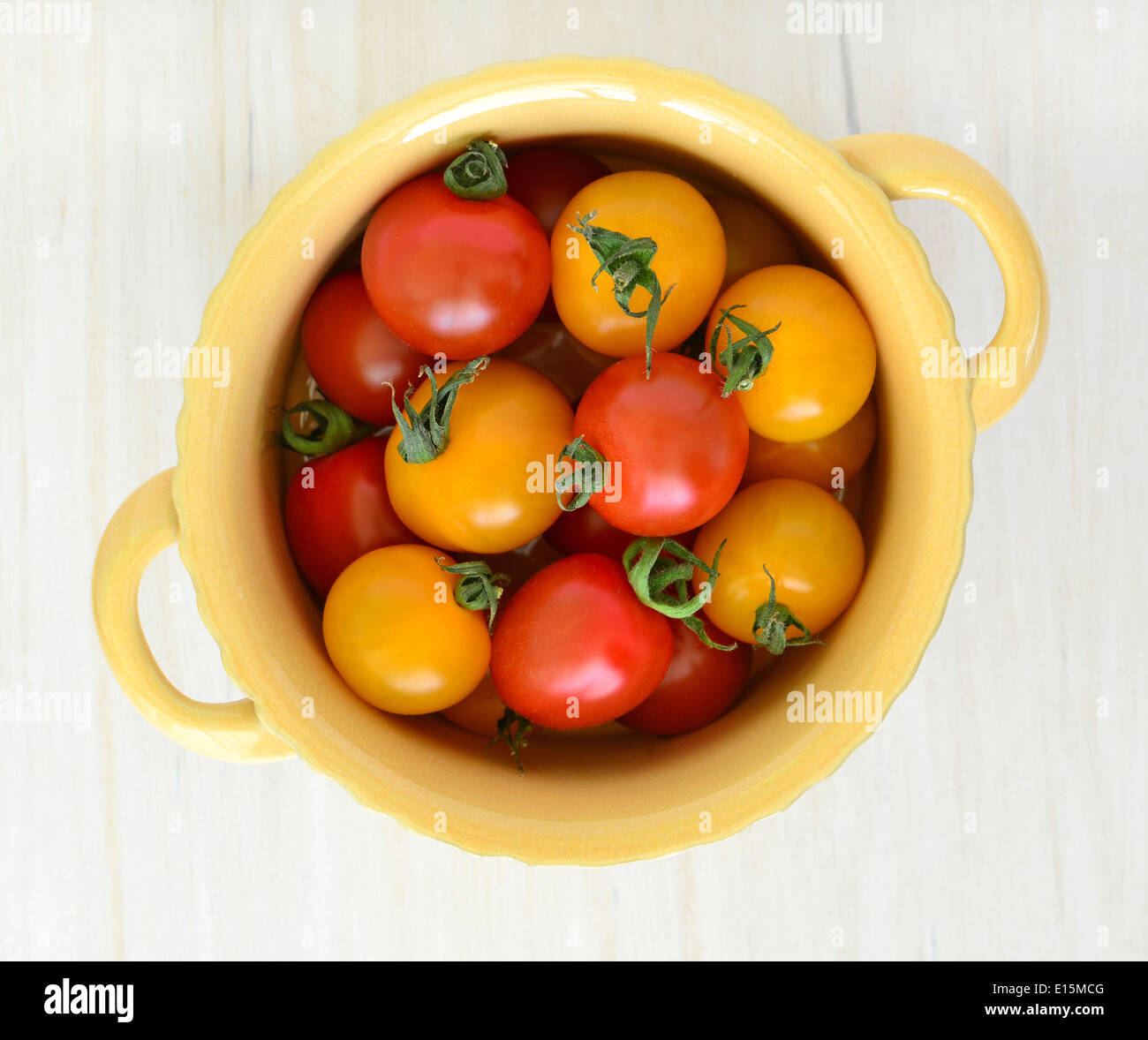 Rote und gelbe Kirschtomaten in gelb von Butterdose mit Griffen auf einem rustikalen weißen Hintergrund von oben geschossen Stockfoto
