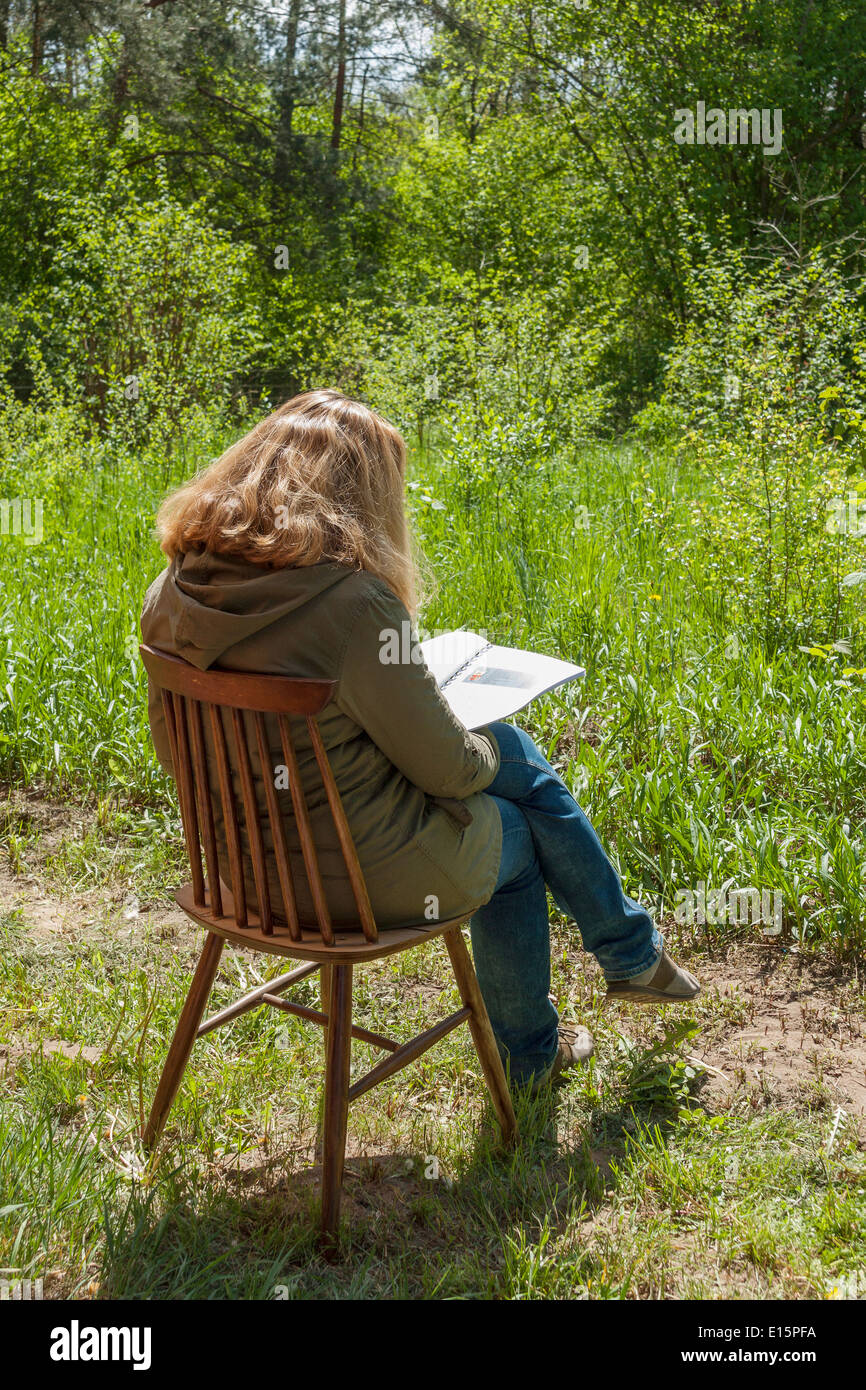 Frau im Freien sitzt auf einem Stuhl und Lesung Stockfoto