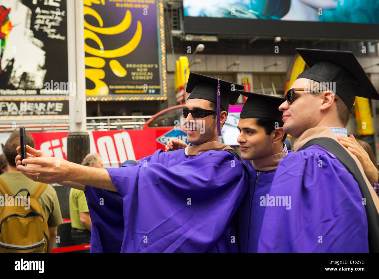 Manhattan, New York, USA - 21. Mai 2014 - In Times Square, drei junge Männer, die Absolvent der New York University School of Business an diesem Tag, sind lila Graduierung Roben und schwarzen Quaste Hüte tragen und Selfies fotografieren mit einem Handy in Manhattan. Stockfoto