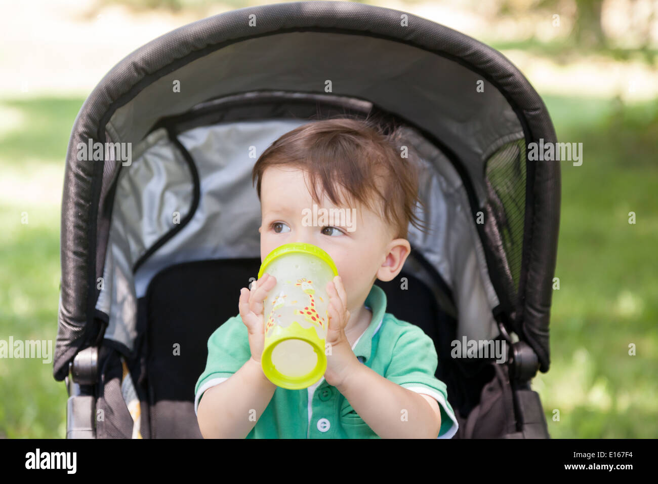 Junge sitzt in einem Kinderwagen und Trinkwasser Stockfoto