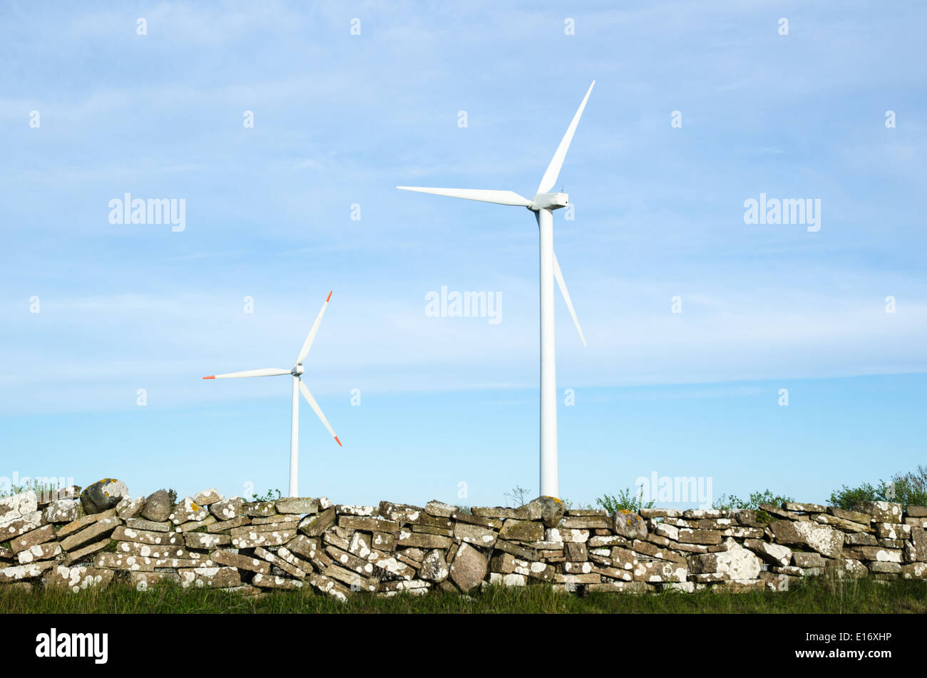 Zwei Wind Turbinen bei blauem Himmel durch ein altes traditionelles stonewall an der schwedischen Insel Öland Stockfoto